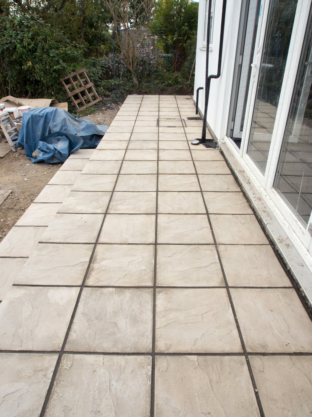 Newly installed tiled patio extending from a white house.