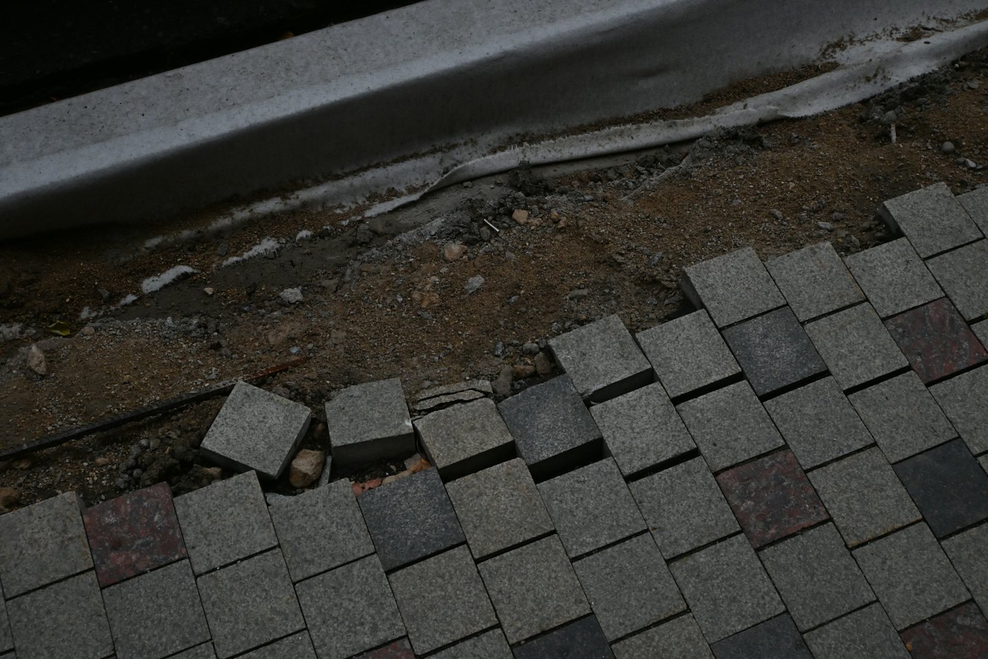 Workers laying grey and brown paving stones next to a curb.