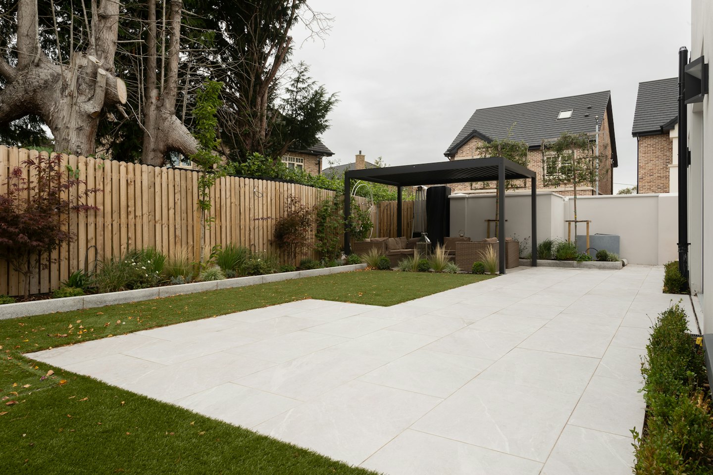 Modern backyard with grey patio, artificial turf, and pergola.
