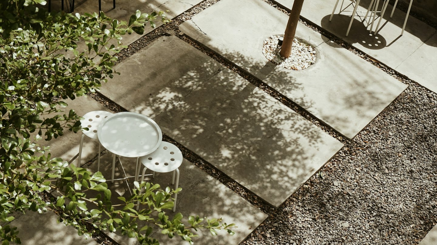 A round white table and stools sit on a paved patio.